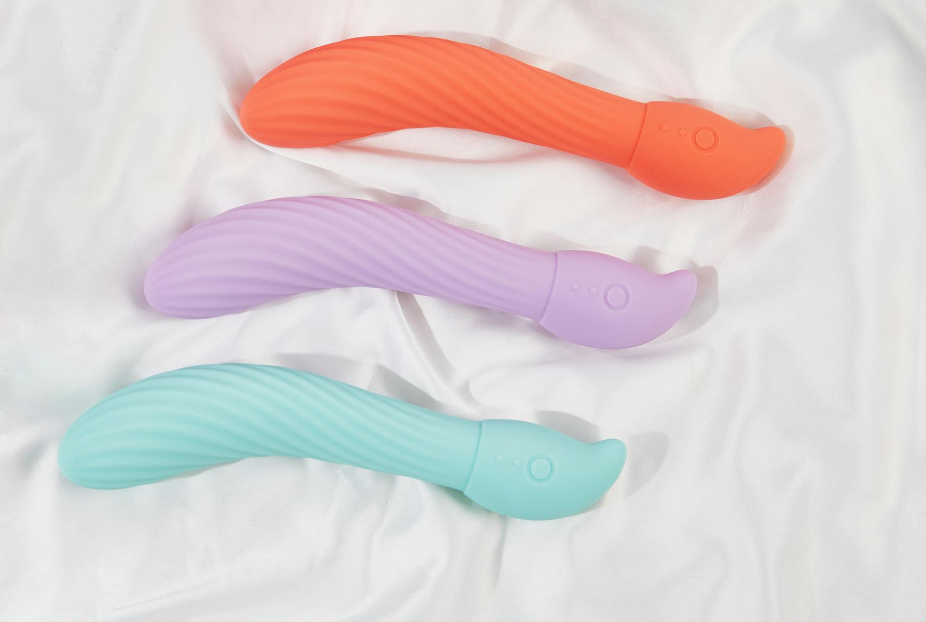 Three colorful clitoral vibrators arranged on white fabric, highlighting their smooth texture and design variations.