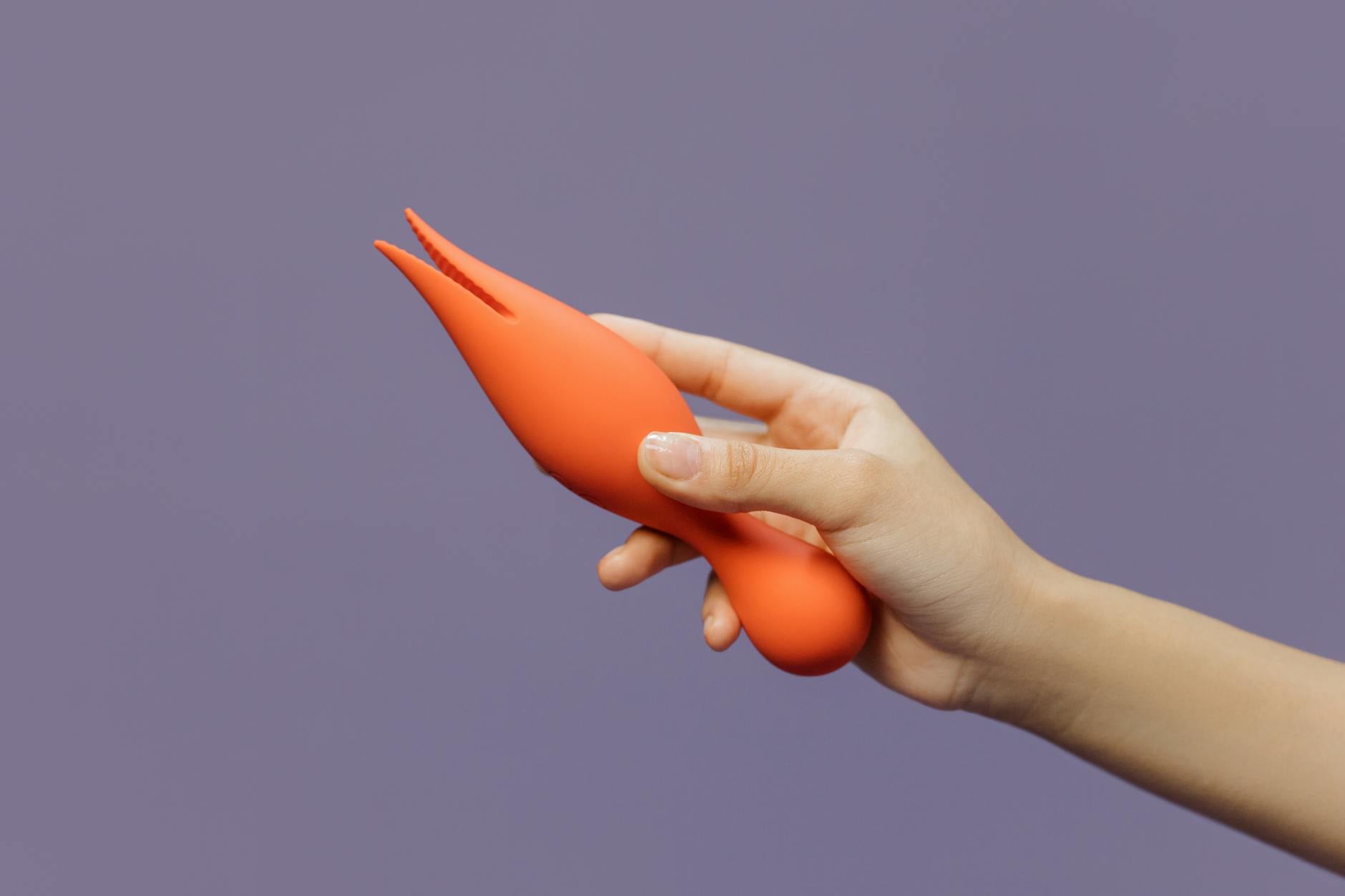 Close-up of a hand holding a lemon clitoral vibrator against a minimalistic purple backdrop