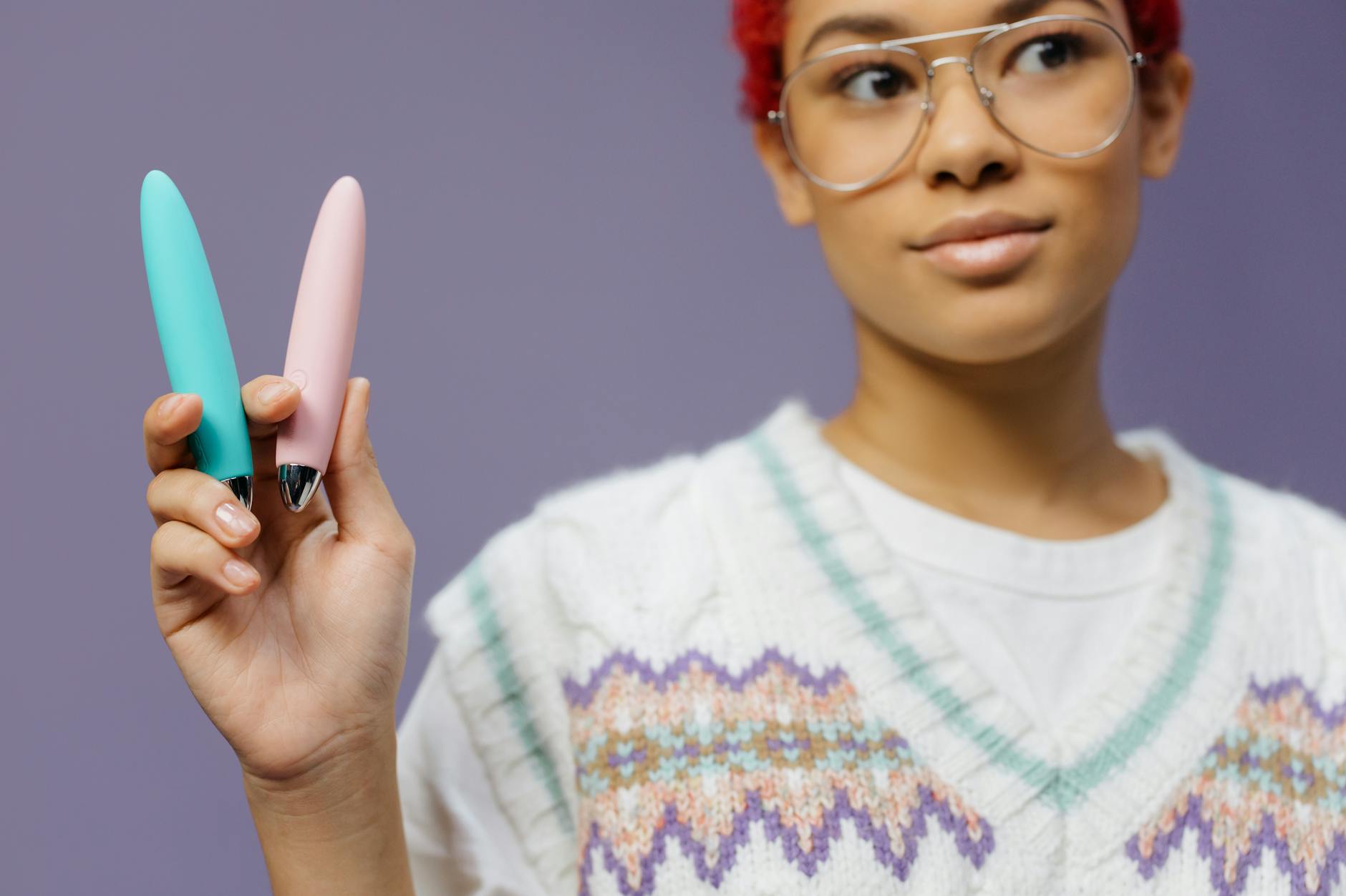 Woman holding vibrators against purple background, reflecting confidence and sexual self-discovery