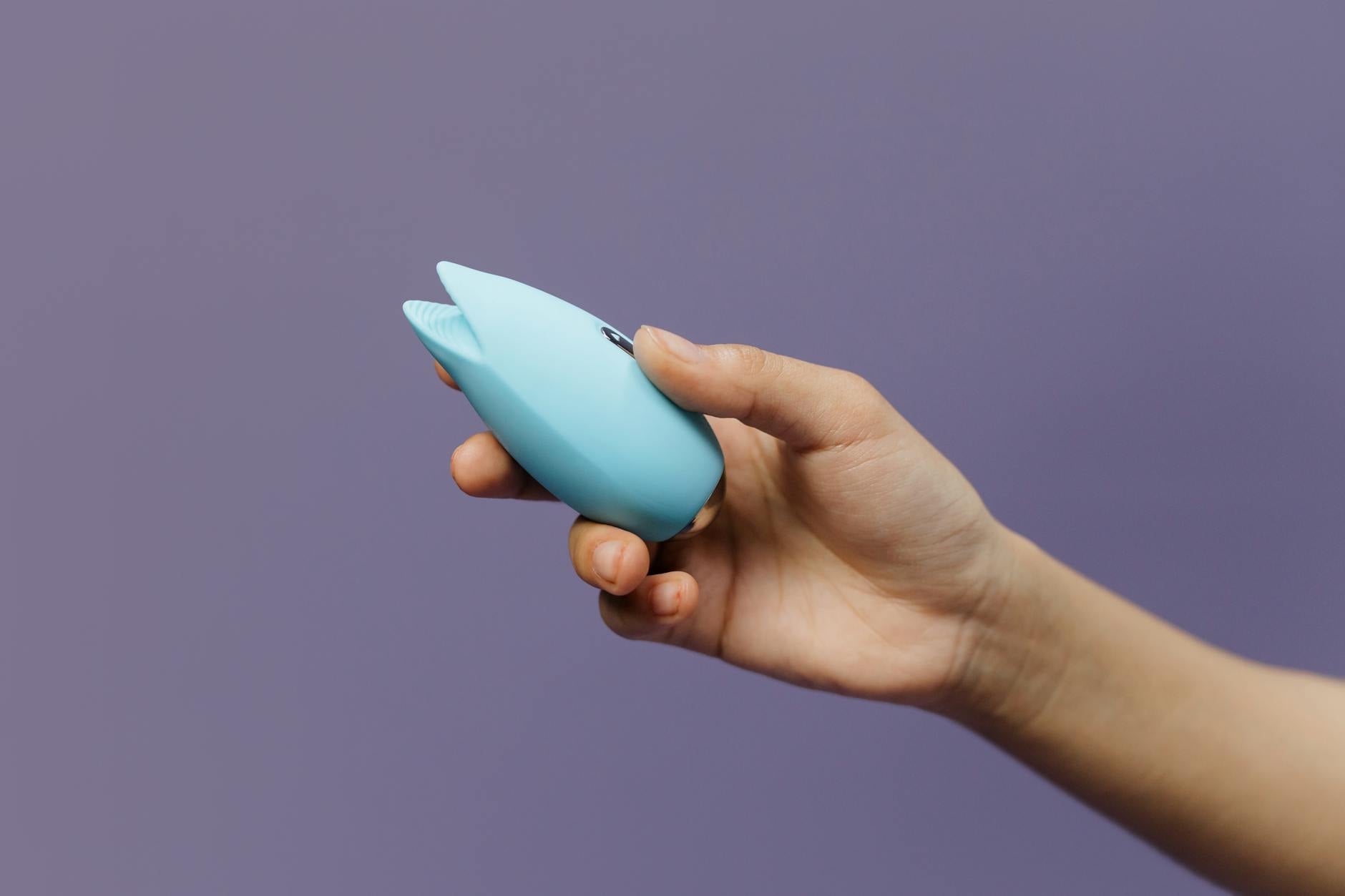 A blue silicone lemon clitoral vibrator held in hand against a purple background