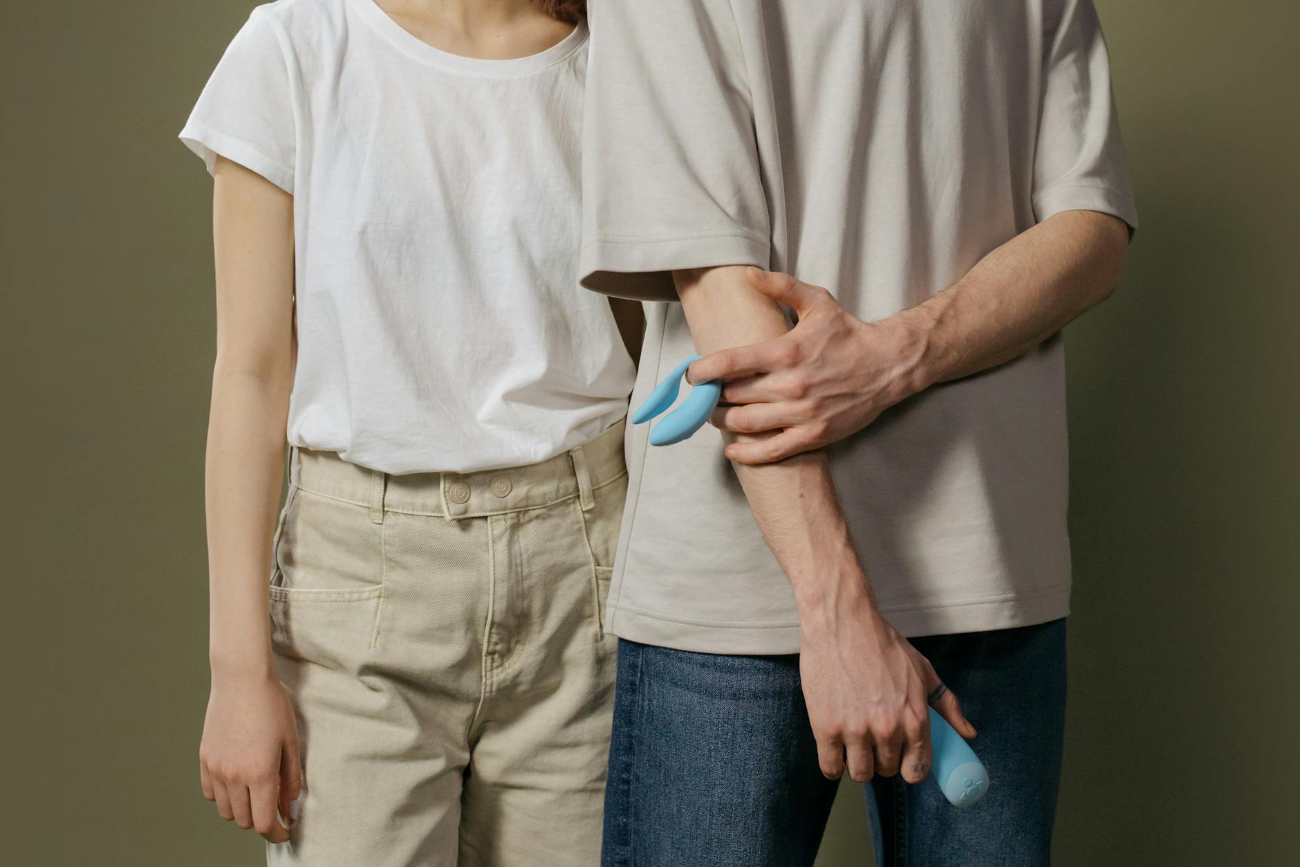 A young couple standing together indoors, holding a blue vibrator, symbolizing modern intimacy and reconnection.